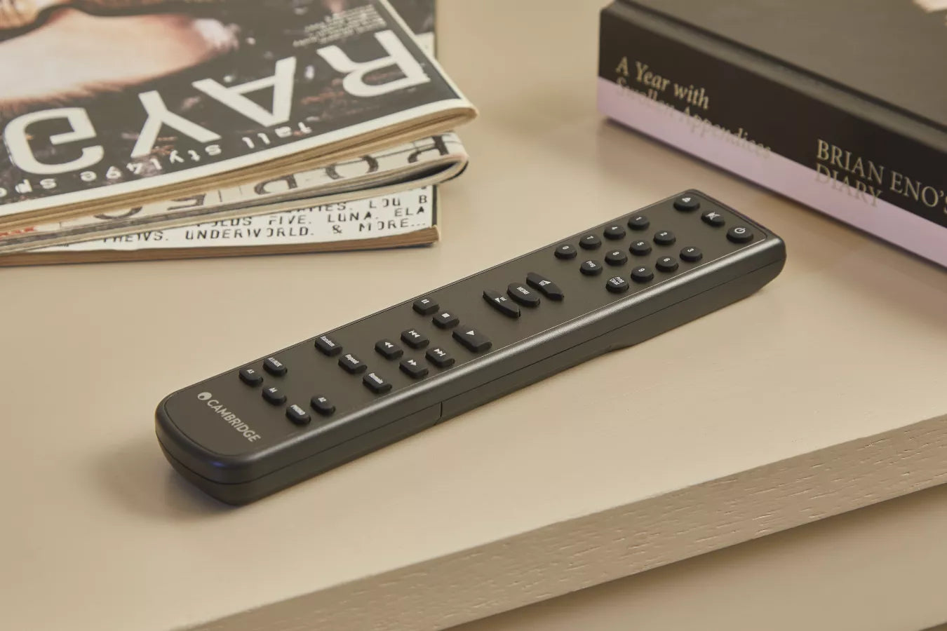 Black remote control on a light wooden surface with books in the background