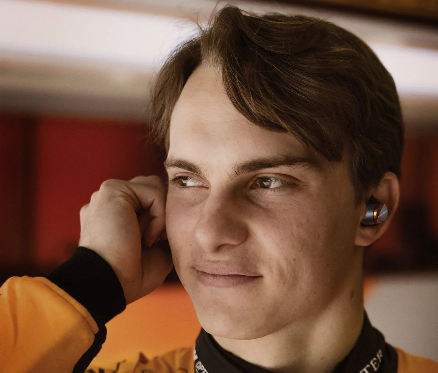 Person wearing a yellow jacket with a blurred backgroun and Bowers & Wilkins PI8, McLaren Edition headphones.