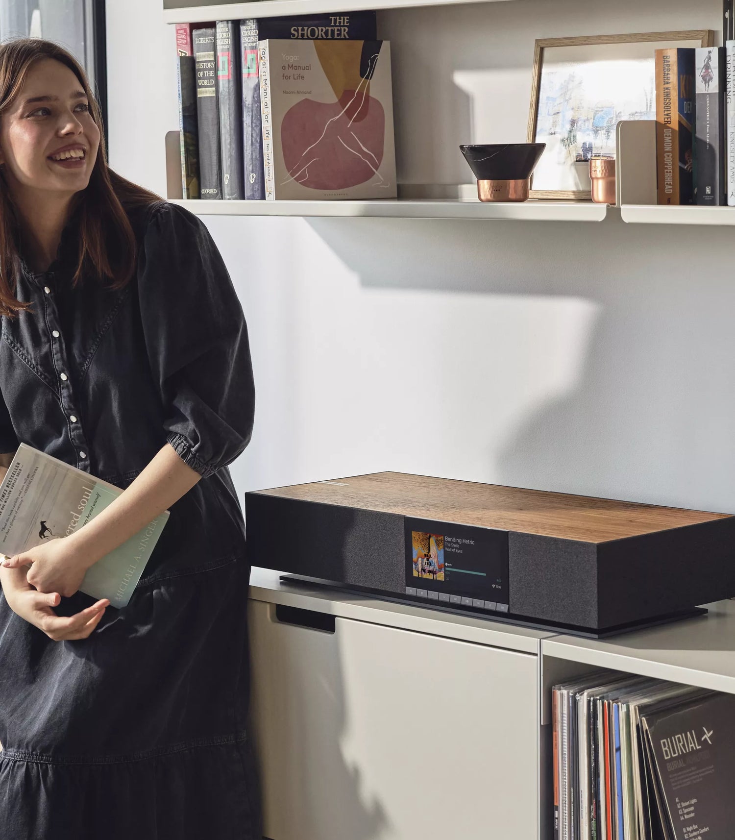 Woman standing next to a Cambridge Audio EVO ONE Music System on a shelf with books and decor