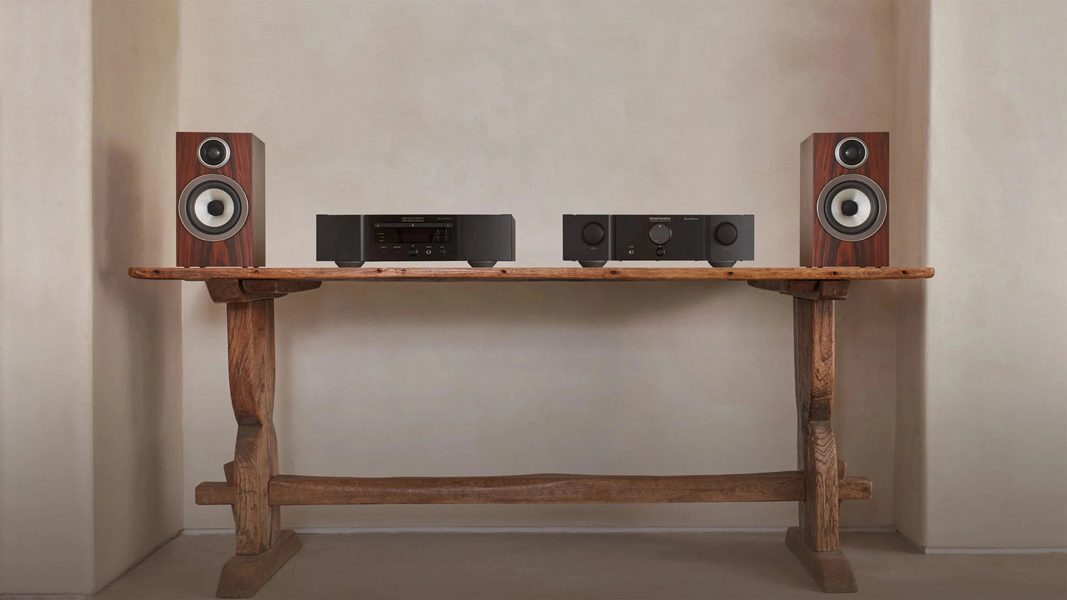 A pair of B&W 707 S3 Bookshelf Speakers in mocha finish placed on a wooden table next to a hifi system.