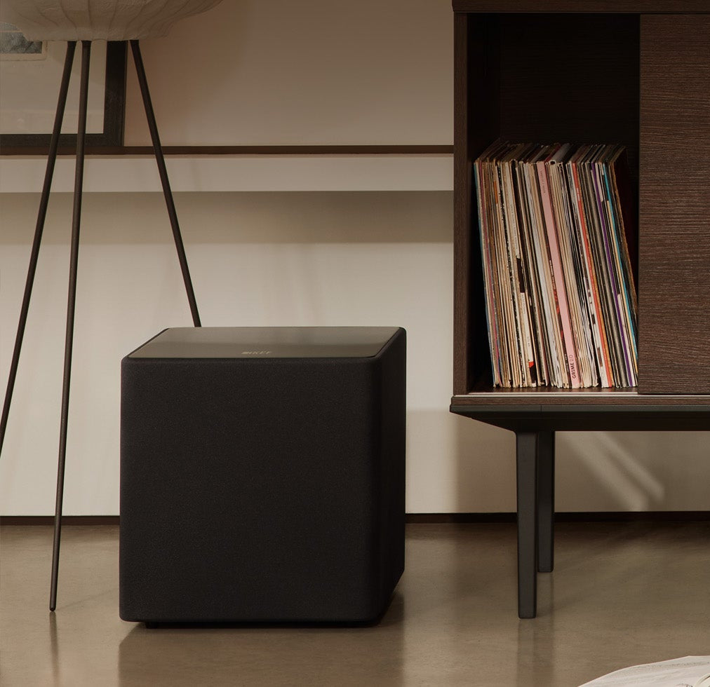 Patterned armchair in a room with a bookshelf and small table and a KEF KUBE 10 MIE 10" Subwoofer.