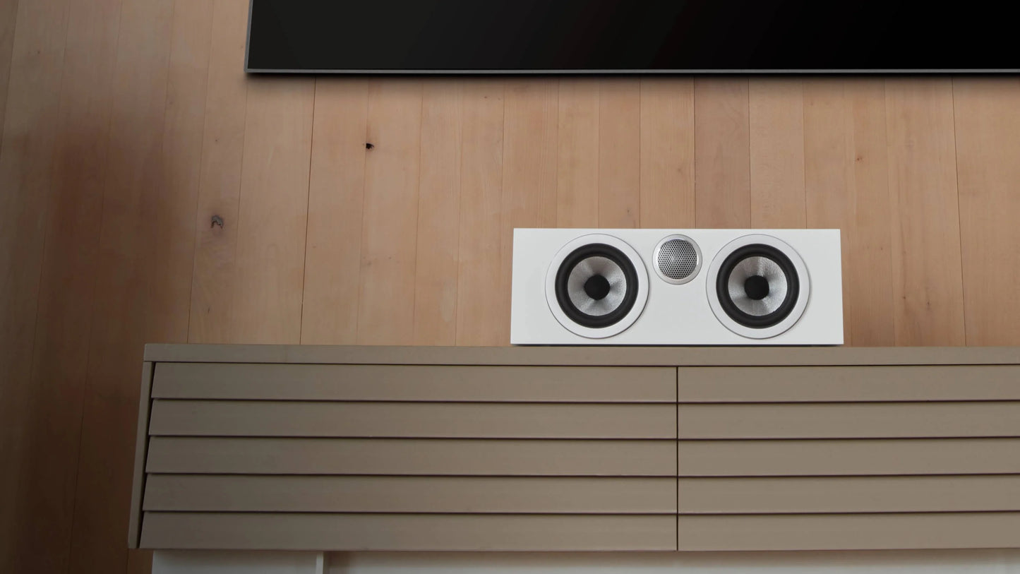 A B&W HTM72 S3 Centre Channel speaker in satin white finish on a TV console in a modern living room.