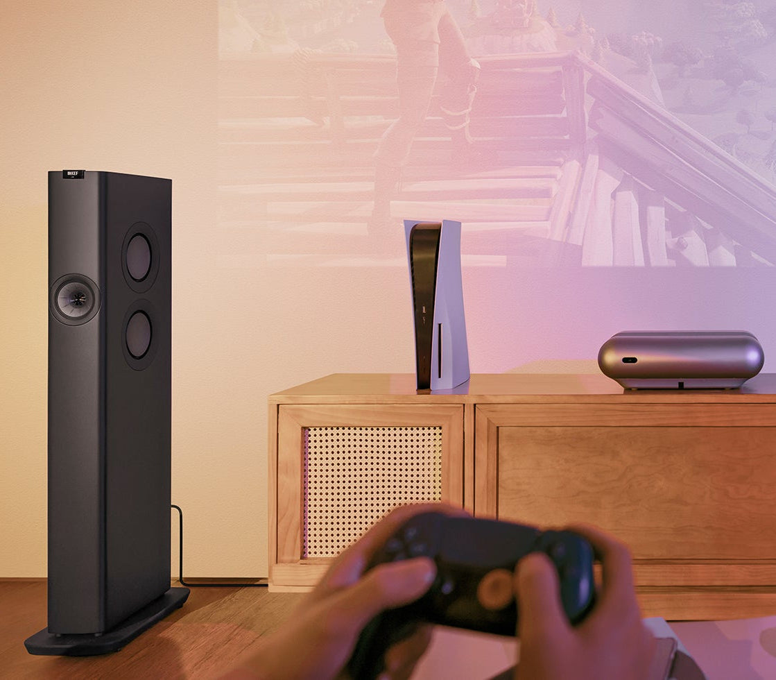 Home theater setup with KEF LS60 Wireless Speakers, TV, and gaming console on a wooden cabinet.