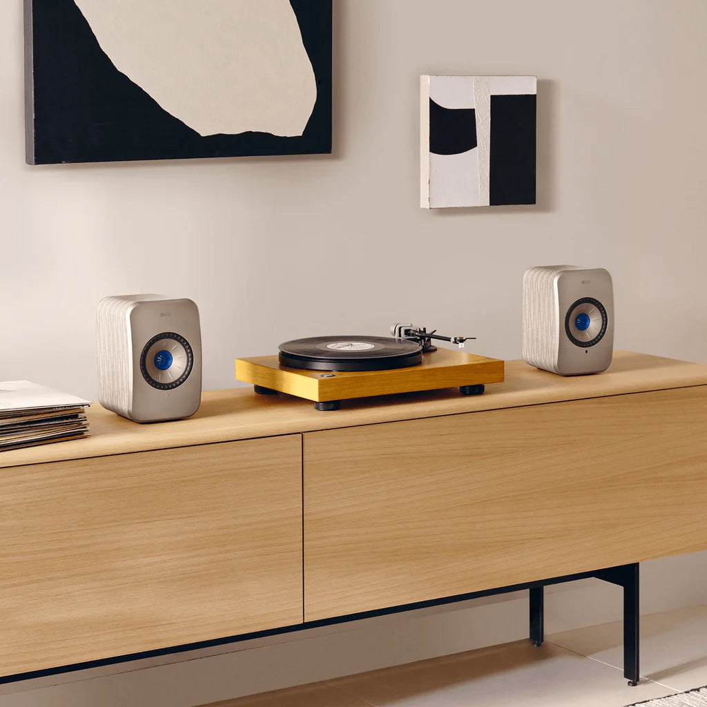 Turntable with KEF LSX II Wireless speakers on a wooden console against a wall with abstract art.