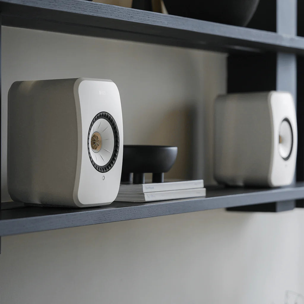 Two gray KEF LSX II Wireless Speakers on a shelf with a blurred background