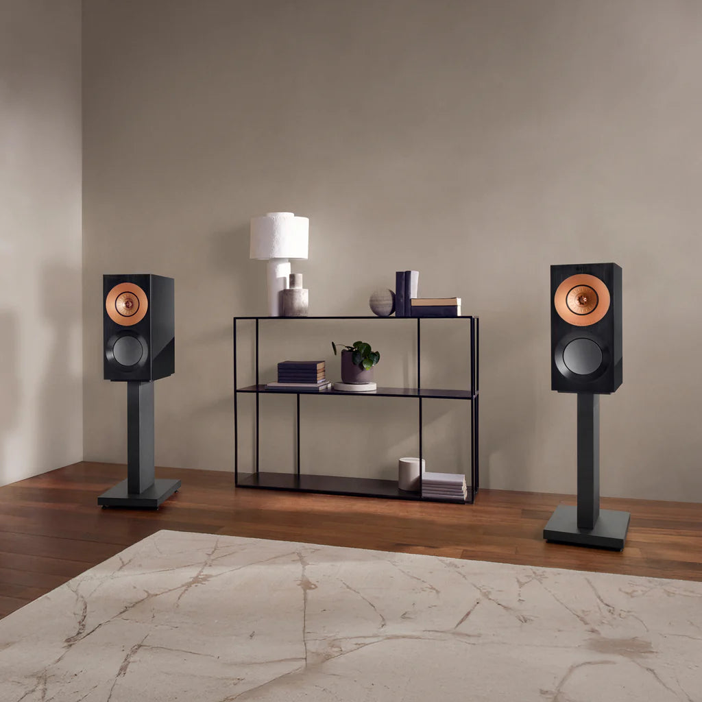 Pair of KEF Reference 1 Meta speakers on stands in a room with a shelf and decor items.