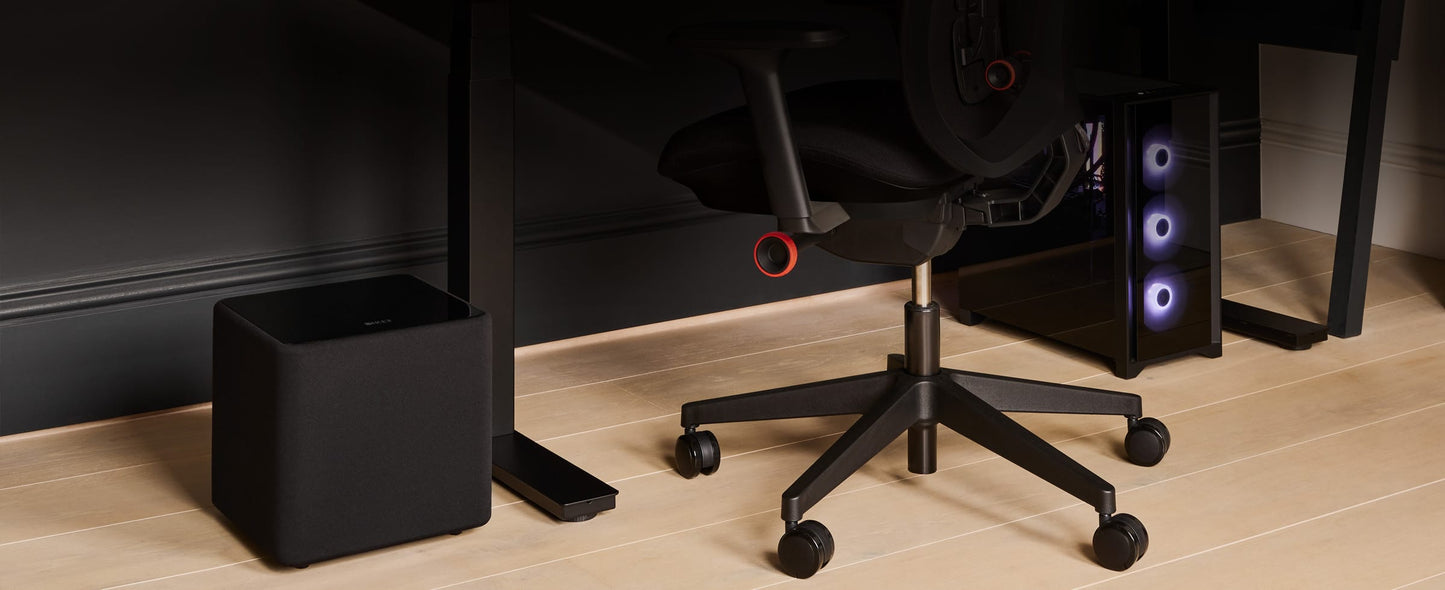 Black office chair with computer equipment and black KEF KUBE 8 MIE 8" Subwoofer on a wooden floor.
