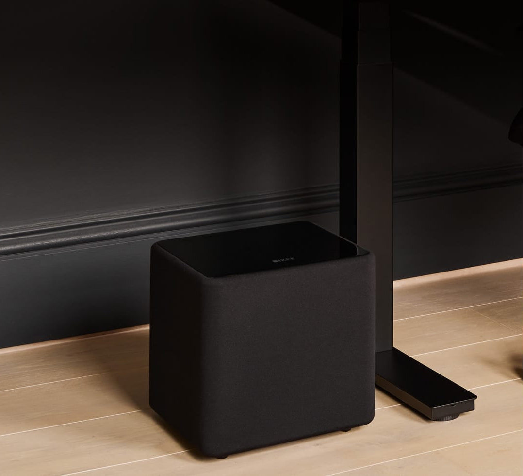 Black office chair with computer equipment and black KEF KUBE 8 MIE 8" Subwoofer on a wooden floor.