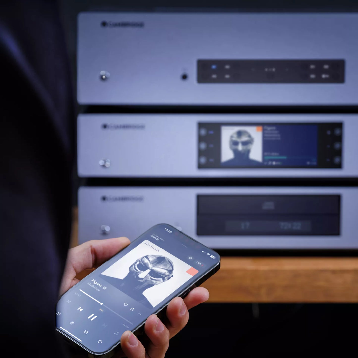 Person using a smartphone to control Cambridge audio equipment with a music app displayed.