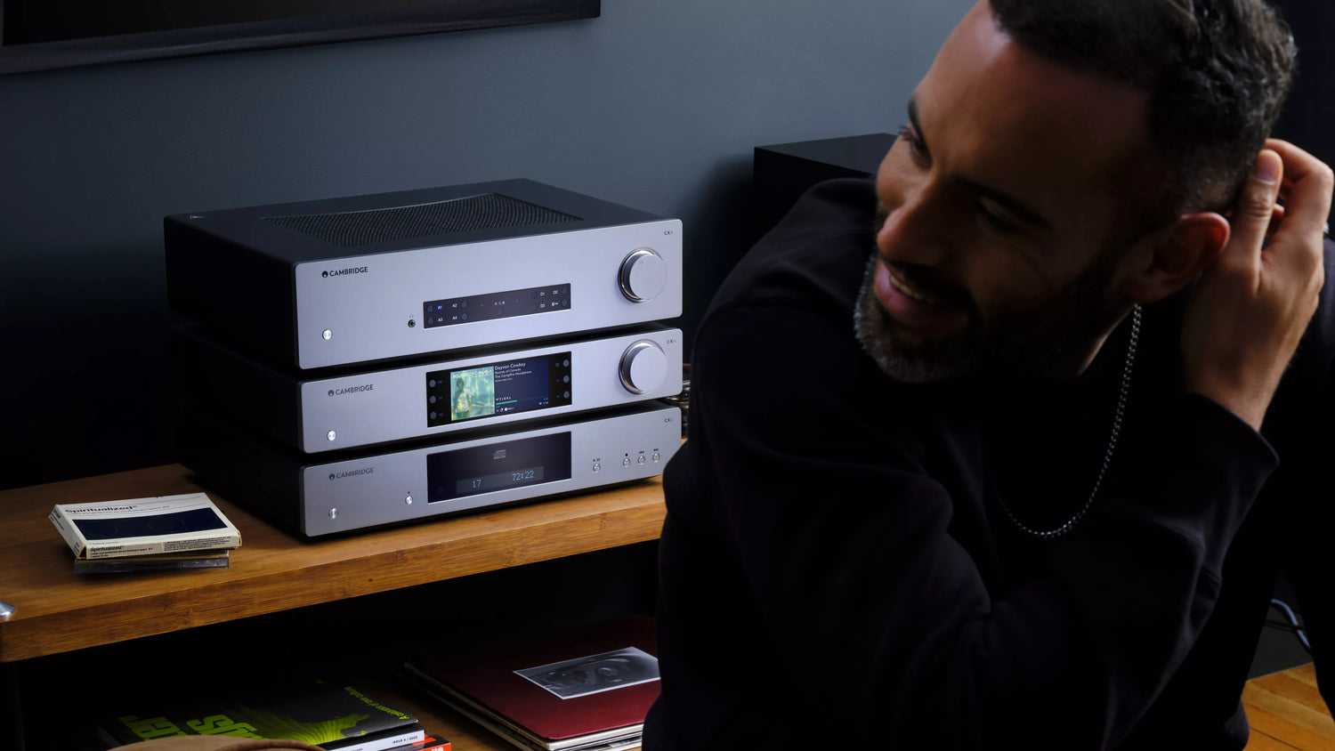 A man sitting in a modern living room in front of a stack of Cambridge audio equipment including Cambridge Audio CXC V2 CD Transport.