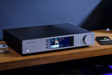 Cambridge Audio CXN100 Network Streaming Player with display and knob on a wooden surface against a dark background