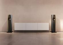 Pair of slim black floor-standing Linn speakers flanking a white audio component in a minimalist room.