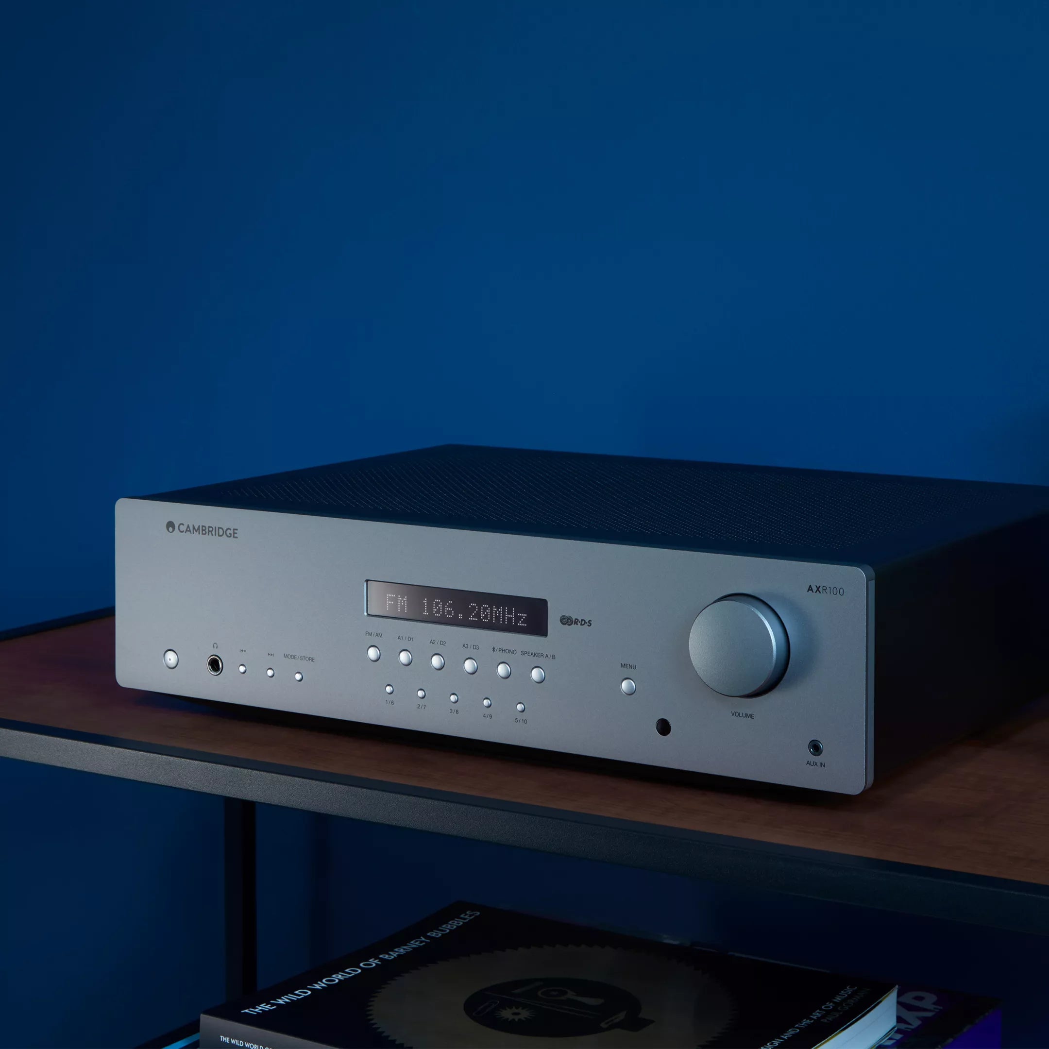 Cambridge Audio AXR100 Stereo Receiver on a wooden shelf with a blue background