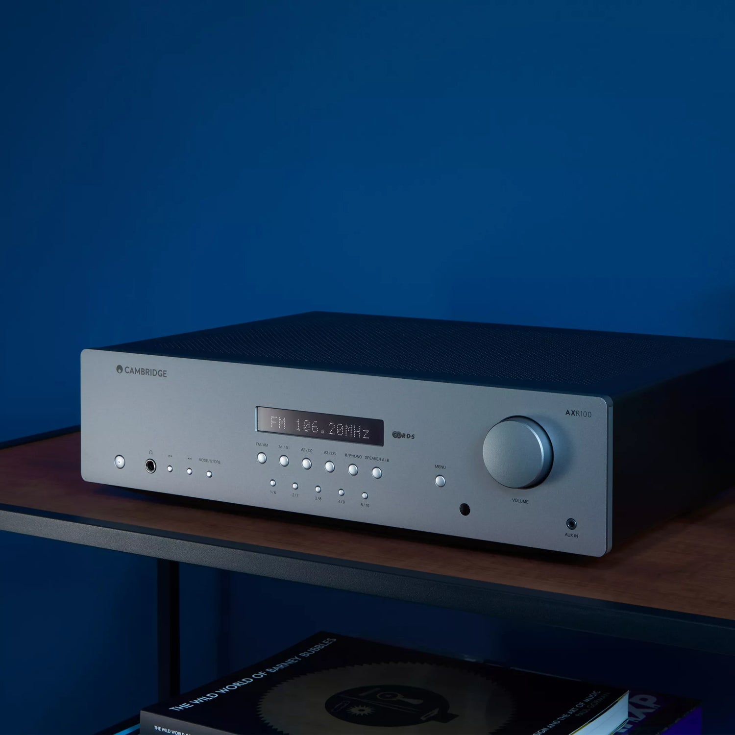 Cambridge Audio AXR100 Stereo Receiver on a wooden shelf with a blue background