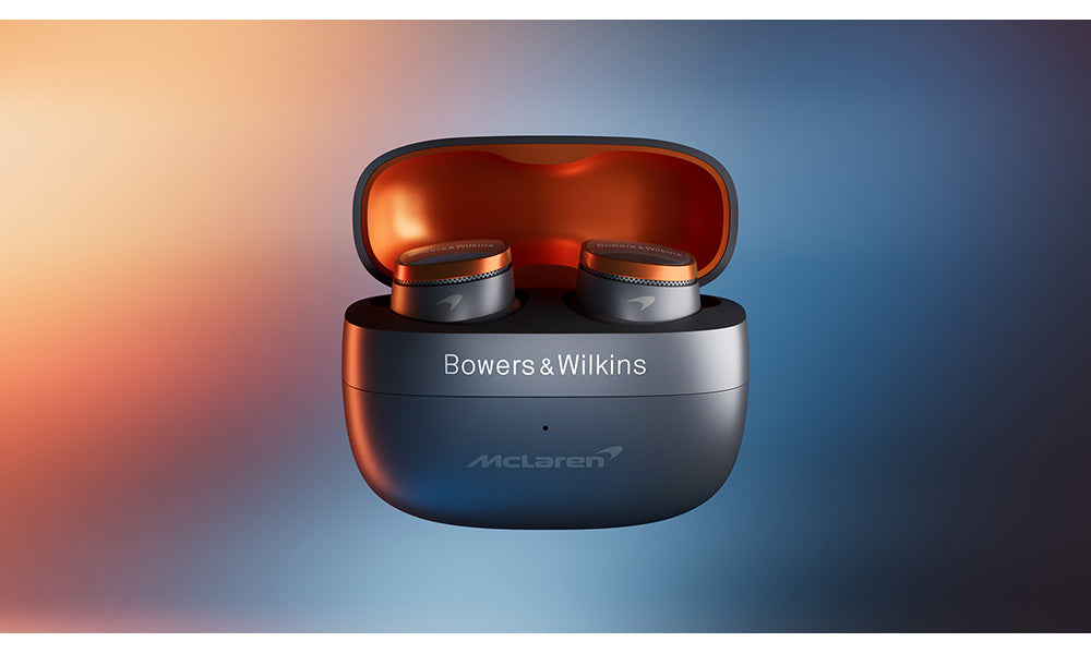 A detail of a pair of Bowers & Wilkins PI8 McLaren Edition in-ear headphones in its travel charging case on a blurred background.