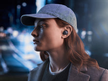 Person wearing a cap and B&W Pi6 True Wireless In-Ear Headphones with a blurred cityscape background