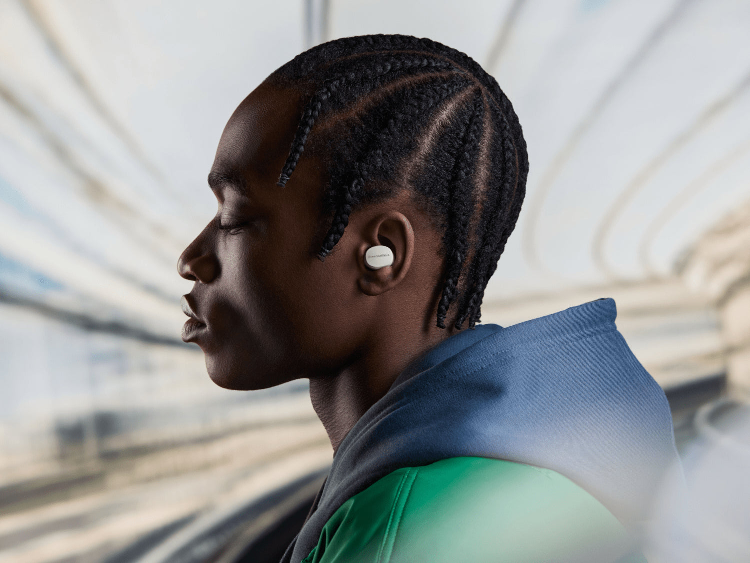 A person wearing B&W Pi6 True Wireless In-Ear Headphones on a blurred cityscape background.