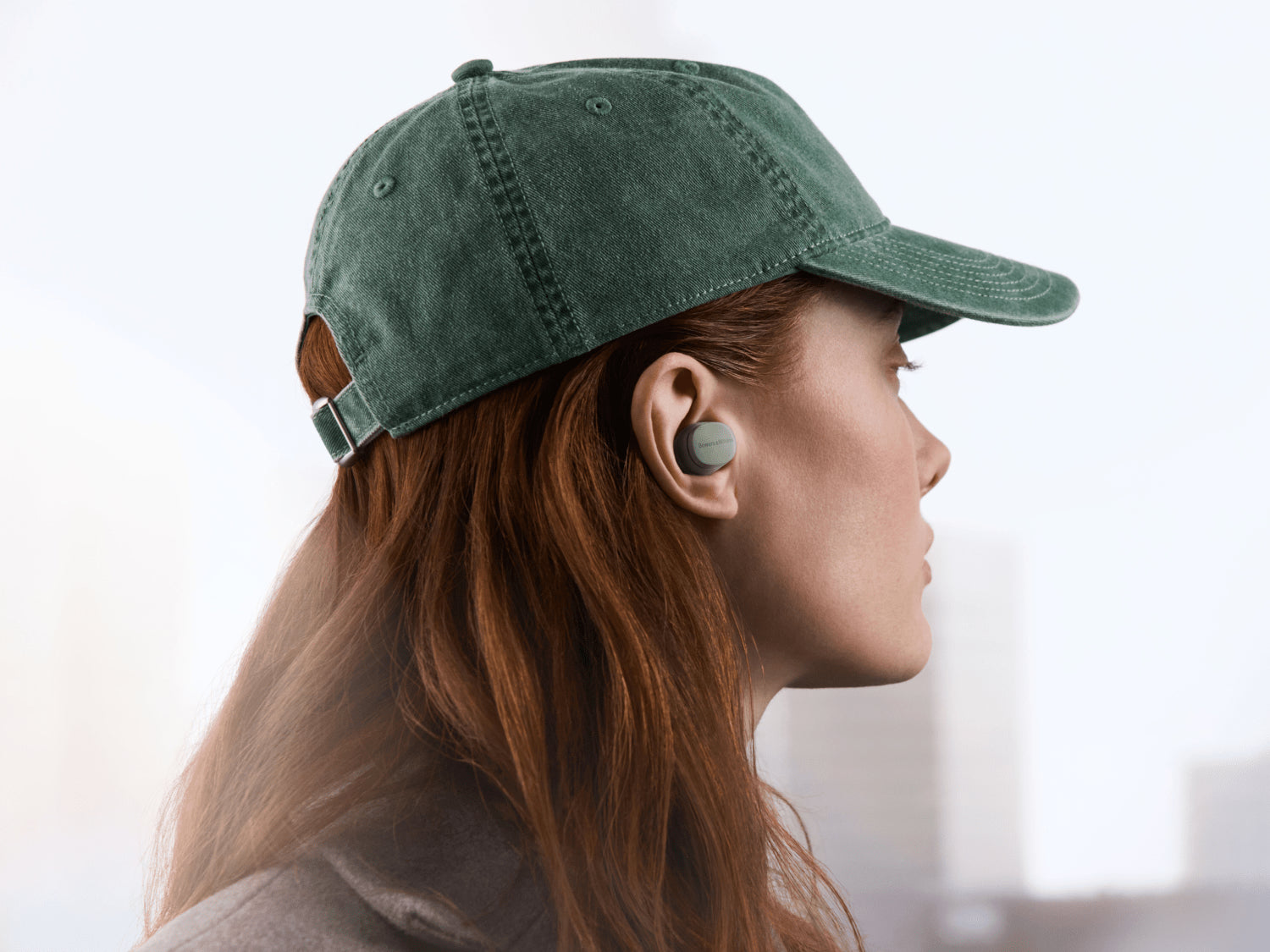 A person wearing a cap and forrest green B&W Pi6 True Wireless In-Ear Headphones.