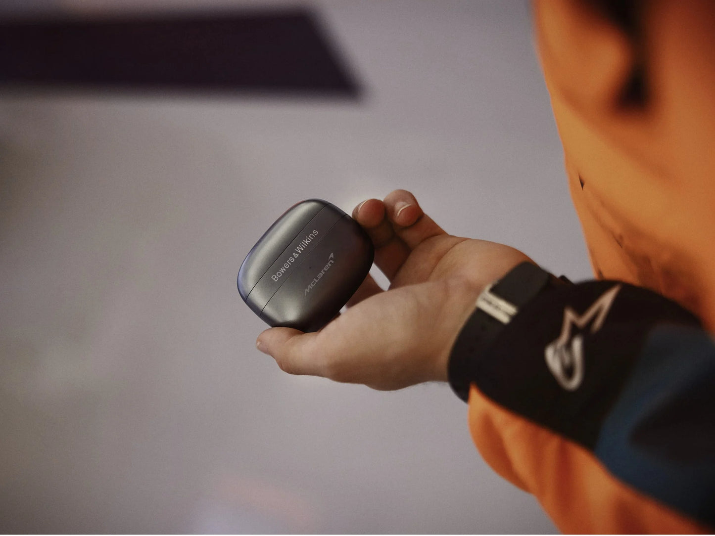 Person holding a small charging case with Bowers & Wilkins PI8, McLaren Edition headphones with a blurred background