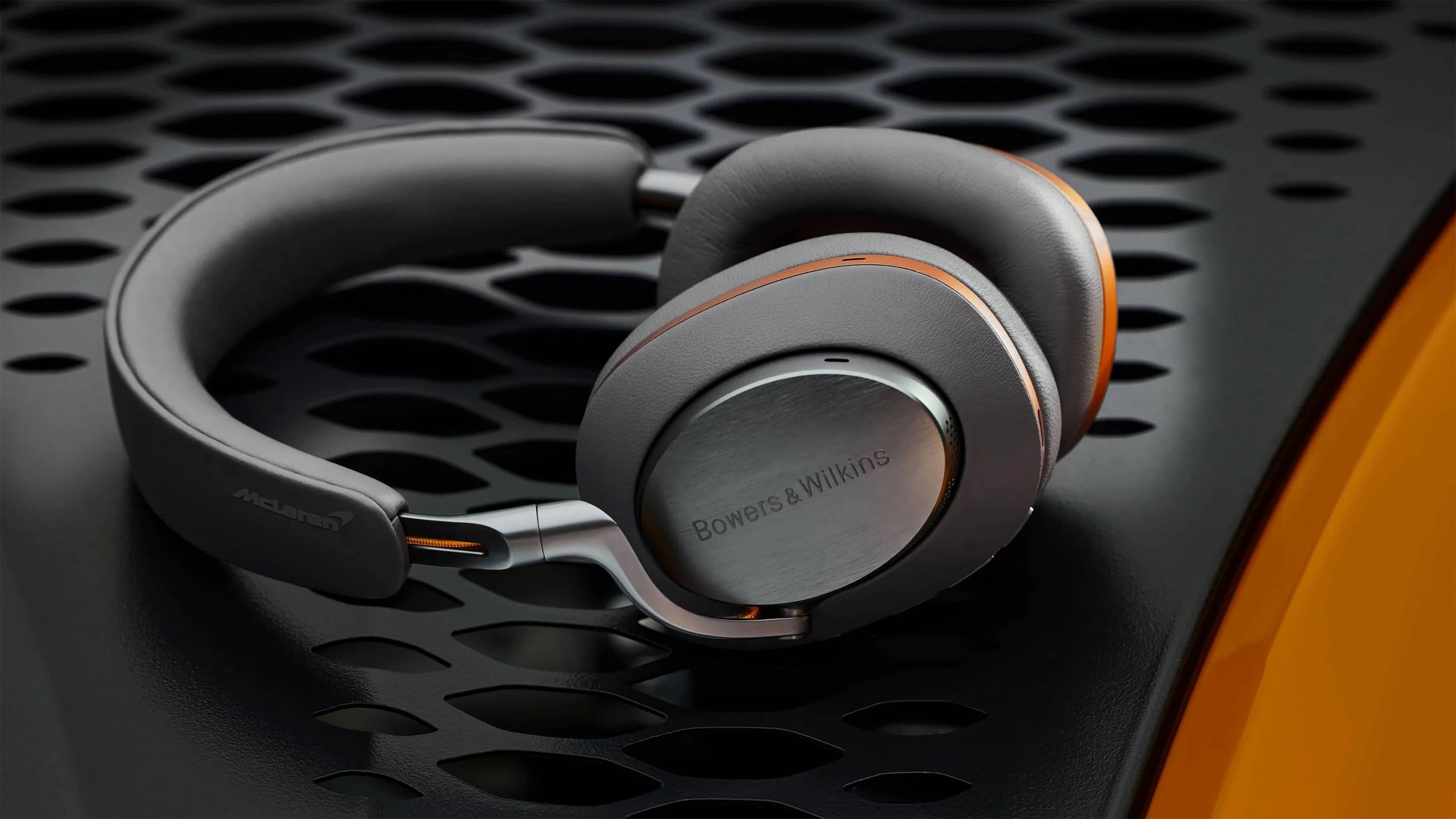 A close-up on Bowers & Wilkins PX8 McLaren Edition Wireless Headphones, featuring Galvanic grey leather with Papaya orange details.