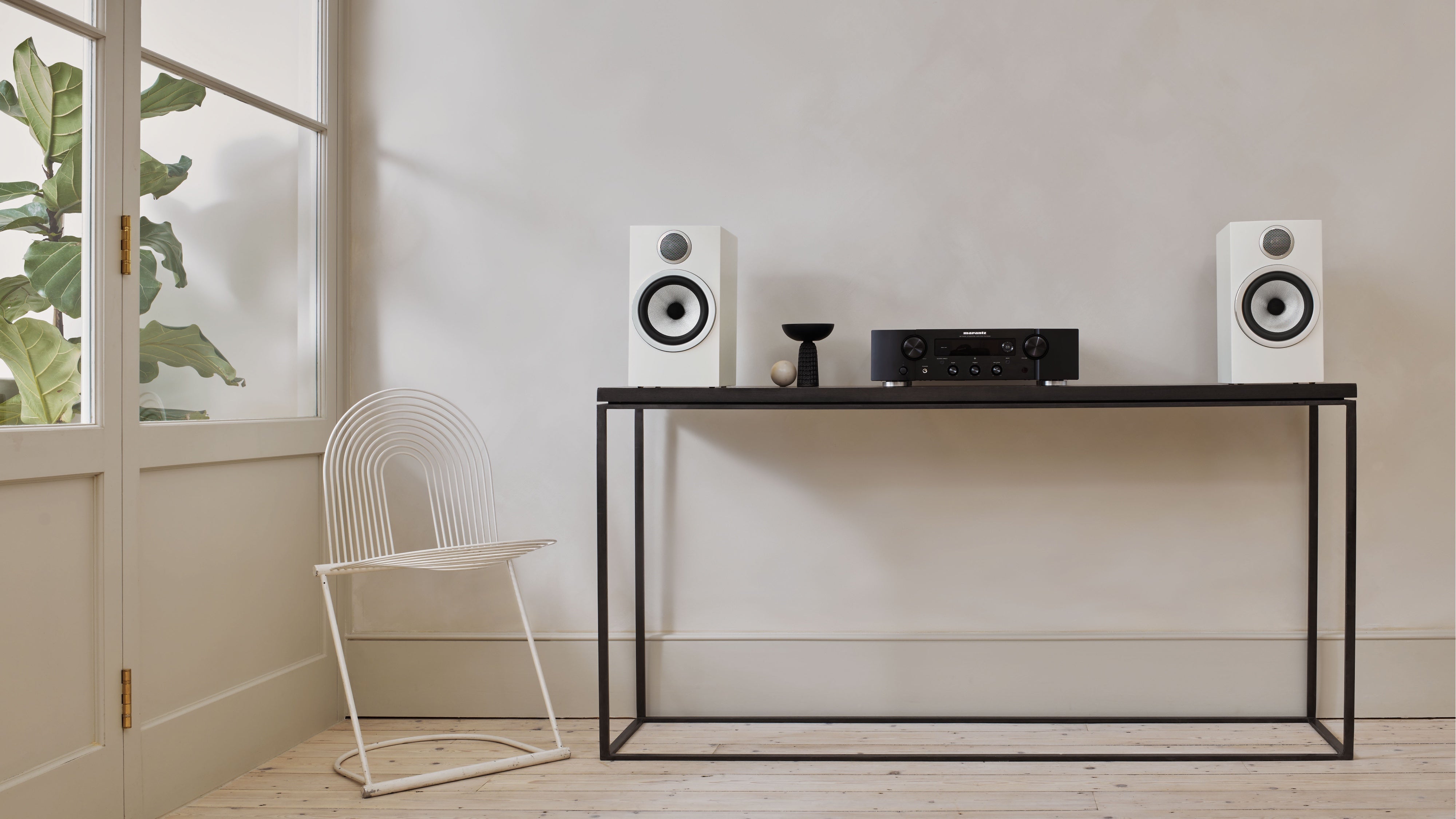 A pair of B&W 706 S3 Bookshelf Speakers in satin white finish on a table in a modern living room.