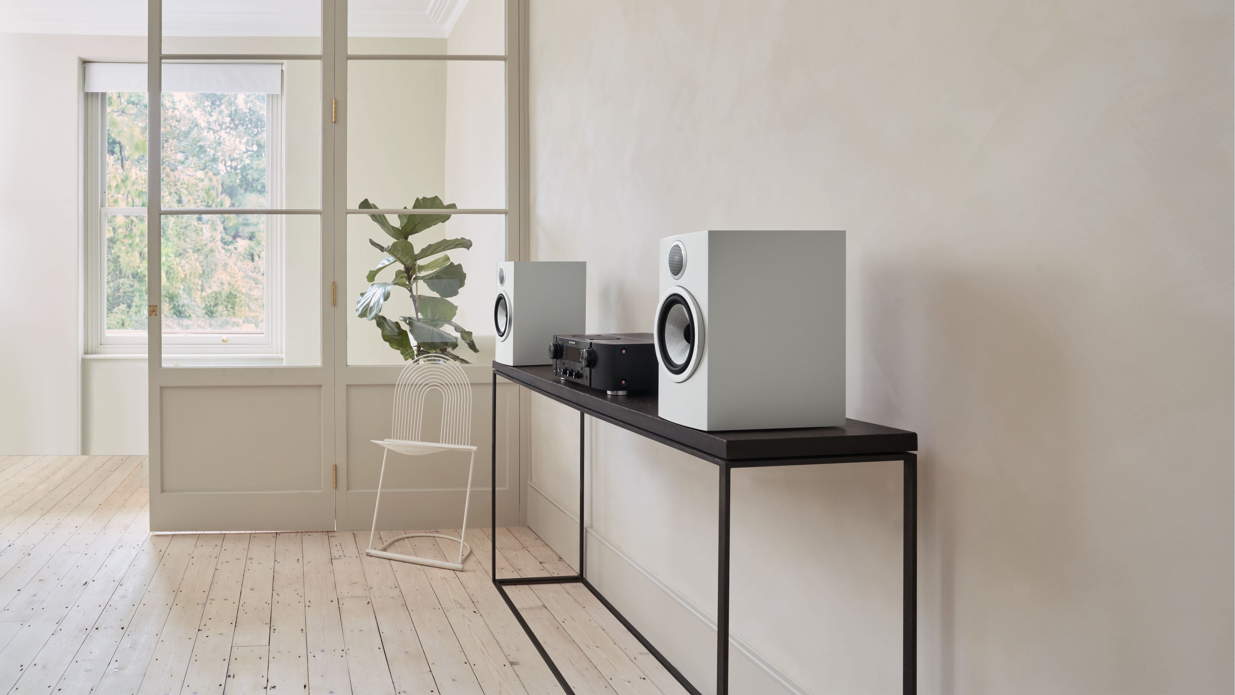 A pair of B&W 706 S3 Bookshelf Speakers in satin white finish on a table in a modern music room.