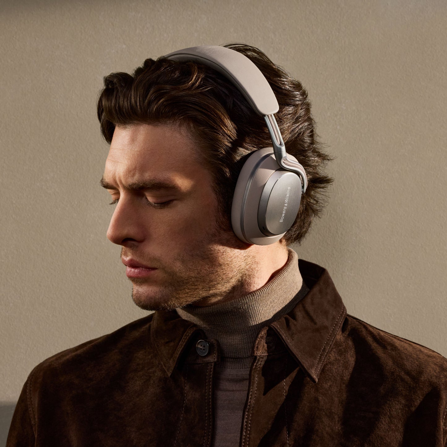 Man wearing gray Bowers & Wilkins PX8 S2 Wireless Headphones against a beige background