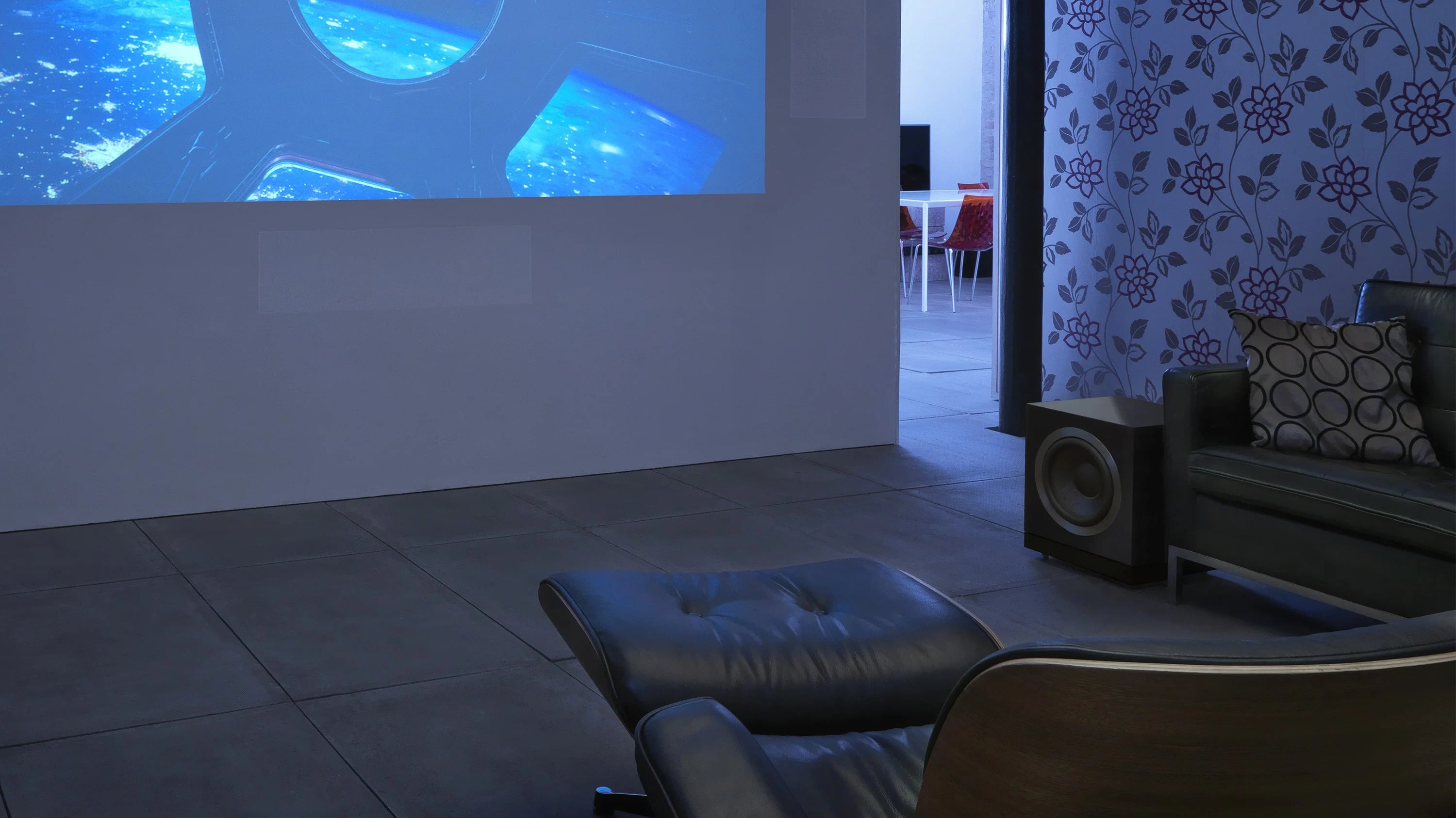 Living room with a projector screen and a B&W DB2D Dual 10'' Subwoofer, surrounded by furniture.