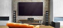 Modern living room with a large flat-screen TV on a brick wall, orange sofa, and speakers and KEF 8b referene subwoofer.
