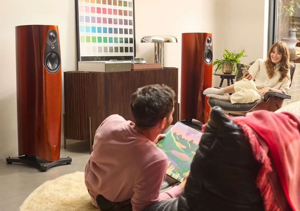 Pair of glossy wood-finish Linn floor-standing speakers with black drivers in a cozy home audio system setup.