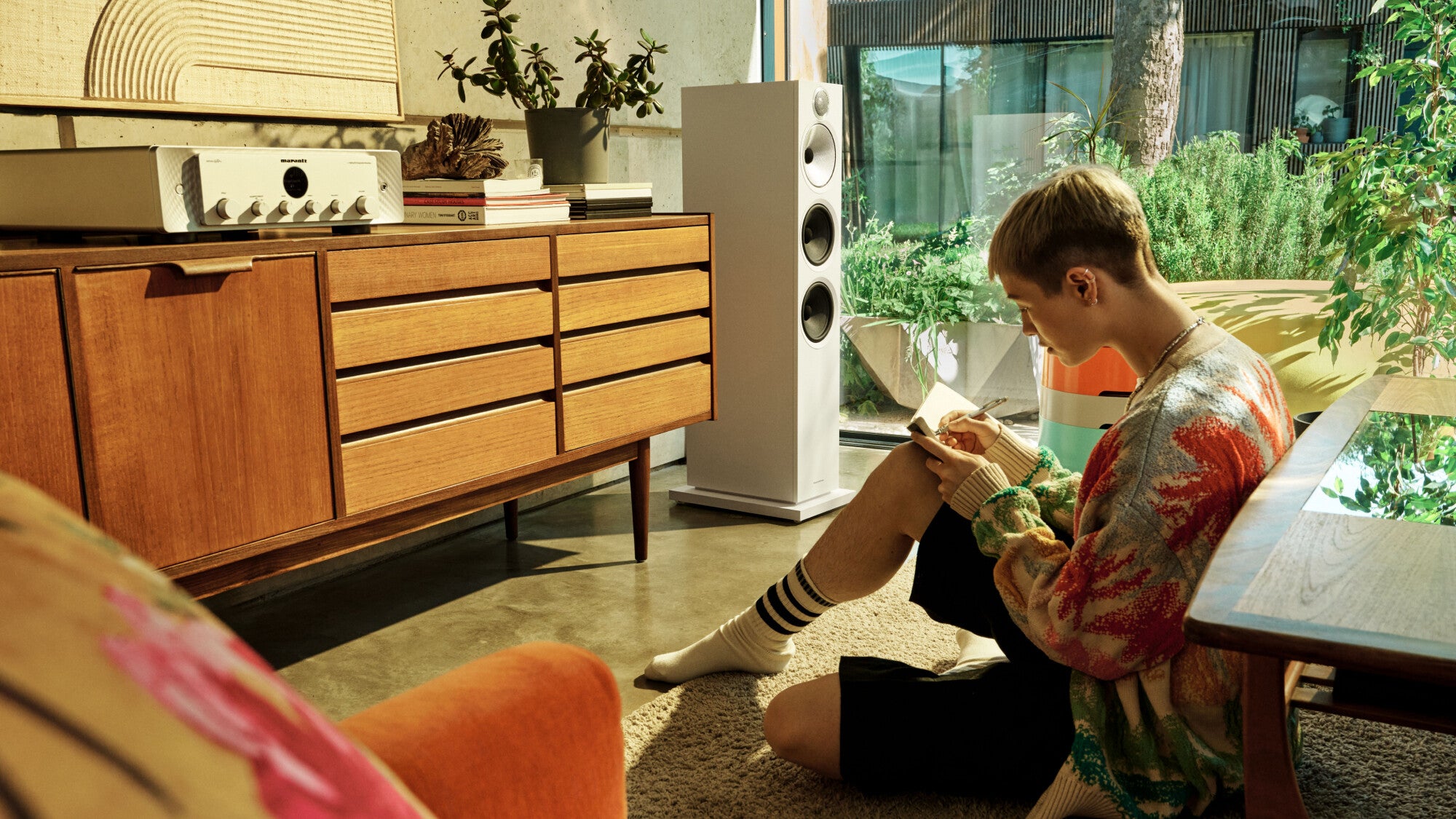 A living room featuring B&W 603 S3 Floor Standing Speaker in white finish and a person writing notes while listening to music