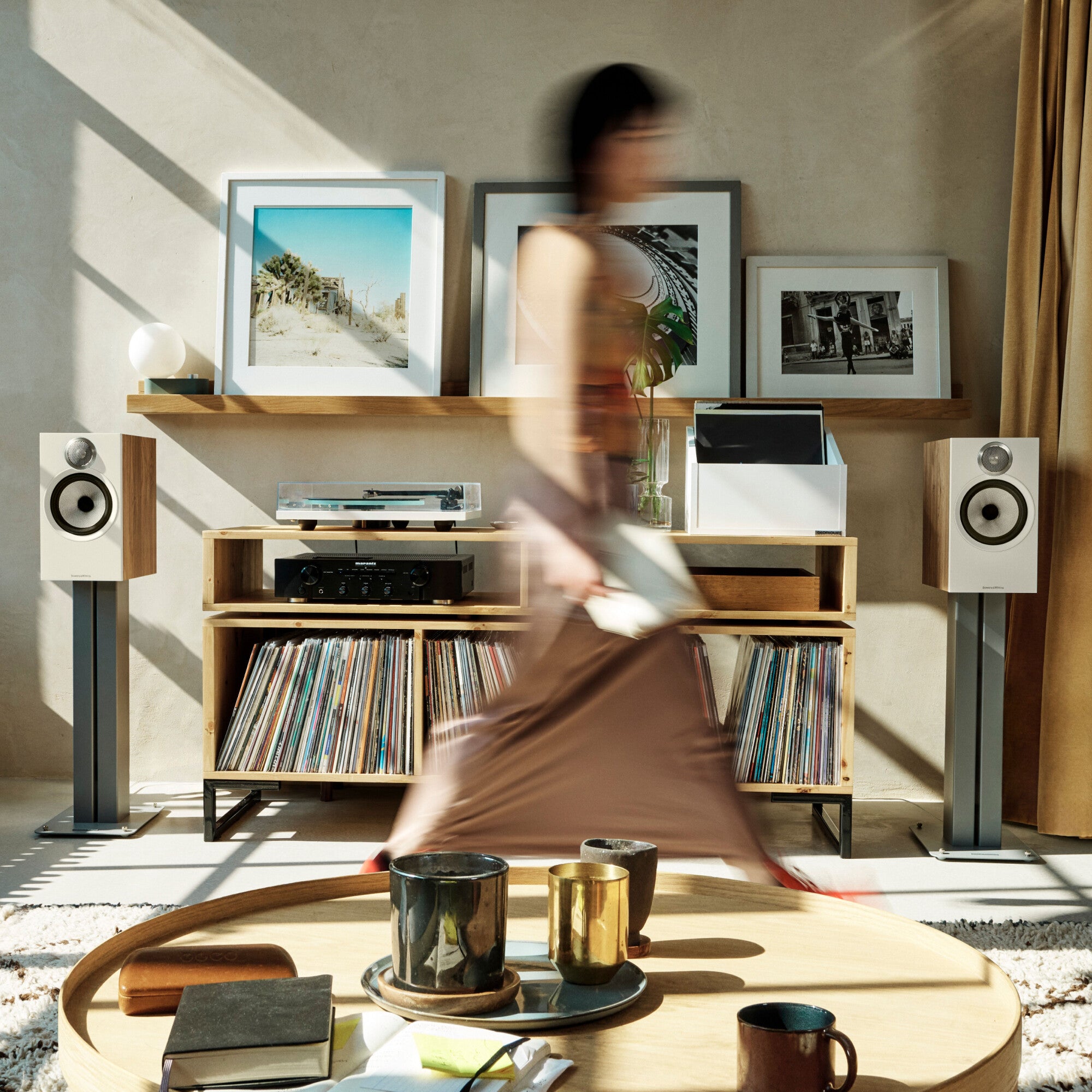 A person walking in front of a pair of B&W 606 S3 Bookshelf Speakers in a modern living room.