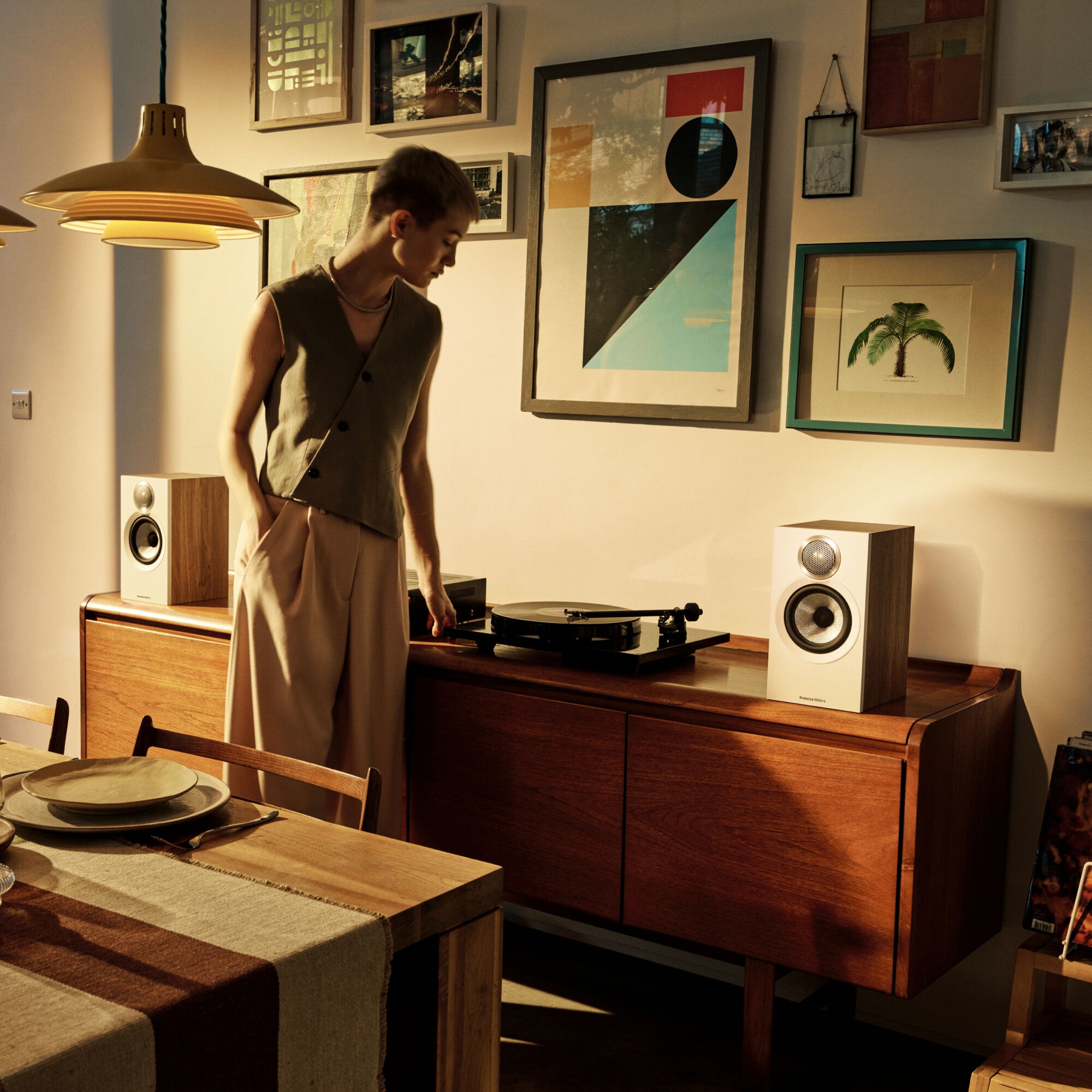 A person looking on a pair of B&W 607 S3 Bookshelf Speakers placed on a shelf in a modern dining room.