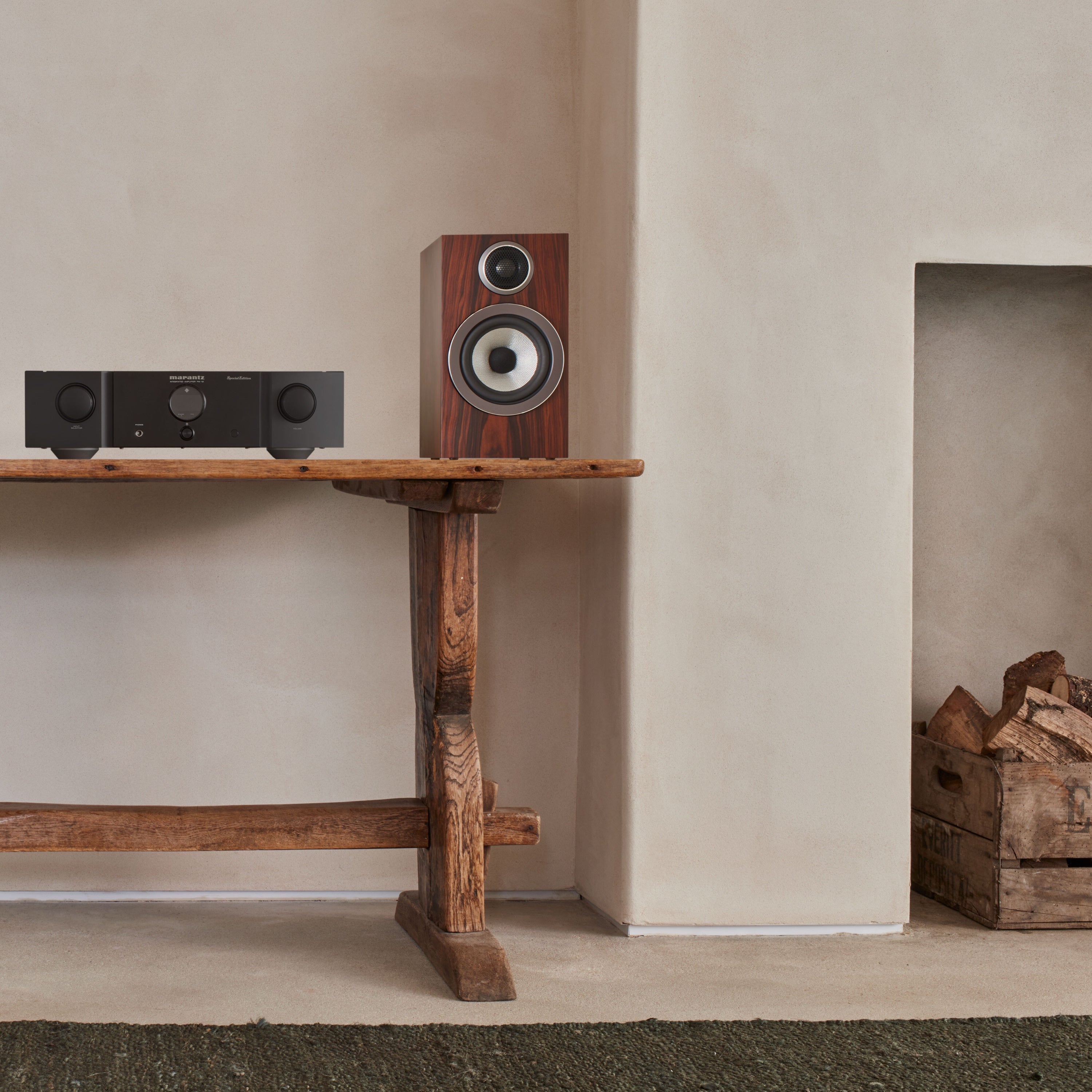 B&W 707 S3 Bookshelf Speaker in mocha finish placed on a table next to a hifi system.