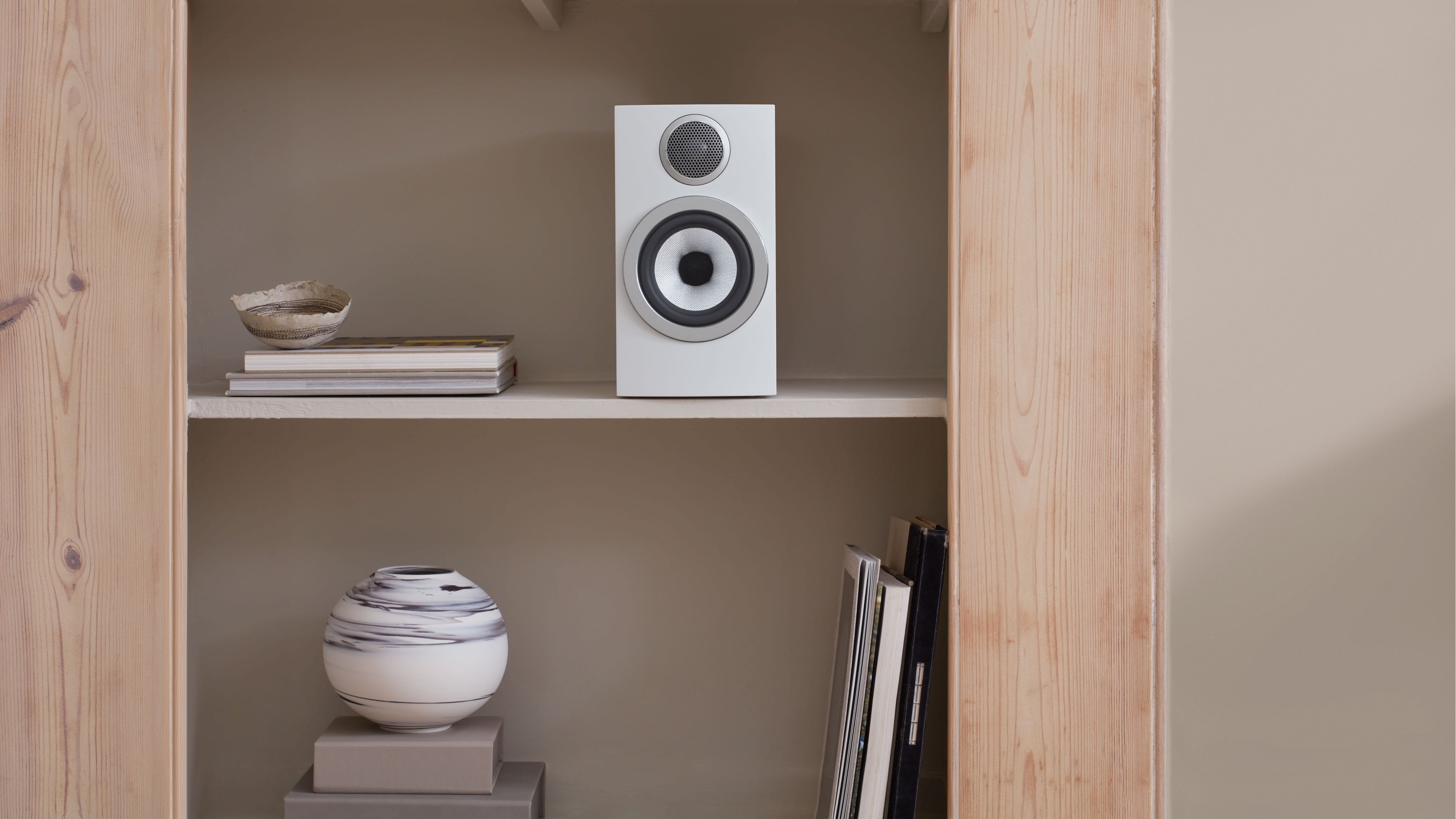 A B&W 707 S3 Bookshelf Speaker in white finish placed on a open modern bookshelf.