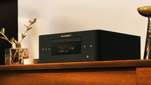 Marantz MCR 60n angled front view on a wooden shelf, OLED display showing Track 1 at 1:54, with warm ambient lighting and decorative accessories