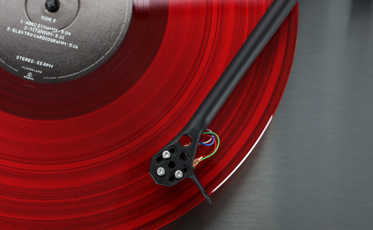 Rega Planar 3 RS turntable with red translucent vinyl record and black tonearm on brushed metal base.