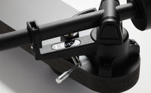 Close-up of a black Rega turntable tonearm and cueing lever, part of a home audio system.