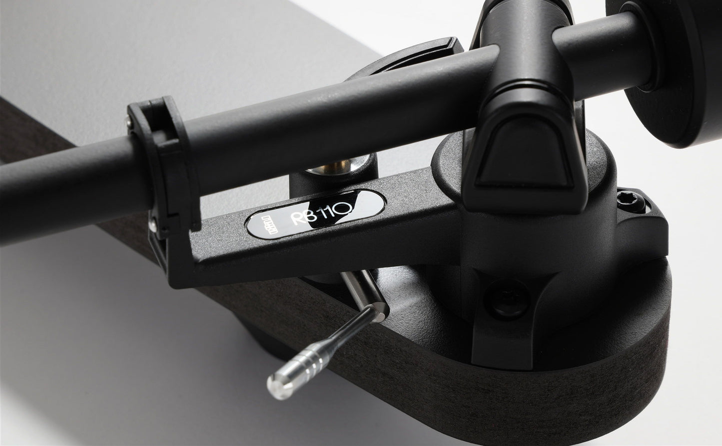 Close-up of a black Rega turntable tonearm and cueing lever, part of a home audio system.