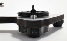 Black Rega turntable with a dark wood plinth, circular platter, tonearm, and front power switch.