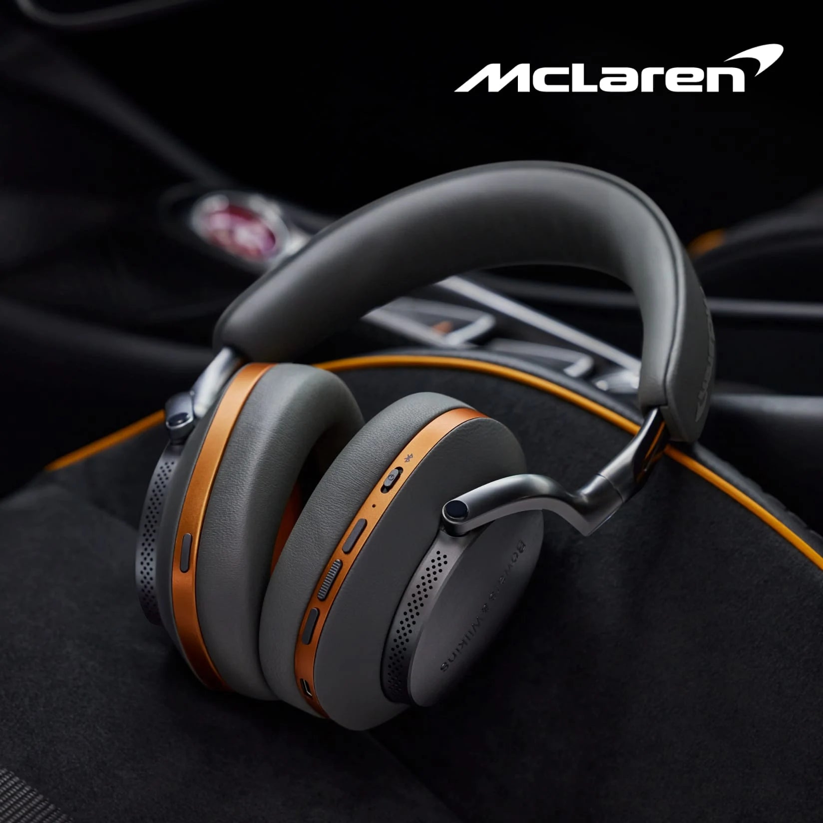 Bowers & Wilkins PX8 McLaren Edition Wireless Headphones, featuring Galvanic grey leather with Papaya orange details placed on a car seat.