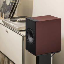Burgundy KEF Coda W Powered Speaker next to a vinyl record player on a beige surface
