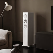 Tall white floor-standing KEF R7 Meta Floor Standing Speaker in a living room setting with a lamp and sofa.