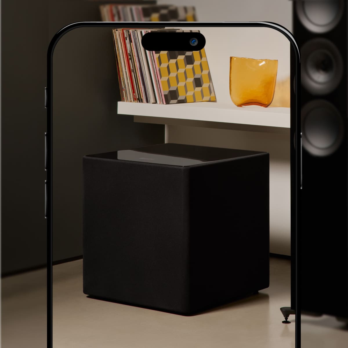 Black cube-shaped KEF KUBE 12 MIE 12" Subwoofer with a shelf above holding books and a glass.