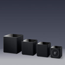 Set of four black square KEF KUBE MIE Subwoofers with varying sizes on a gray background