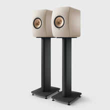 Pair of beige speakers on black KEF S2 Floor Stands for LS Series against a white background