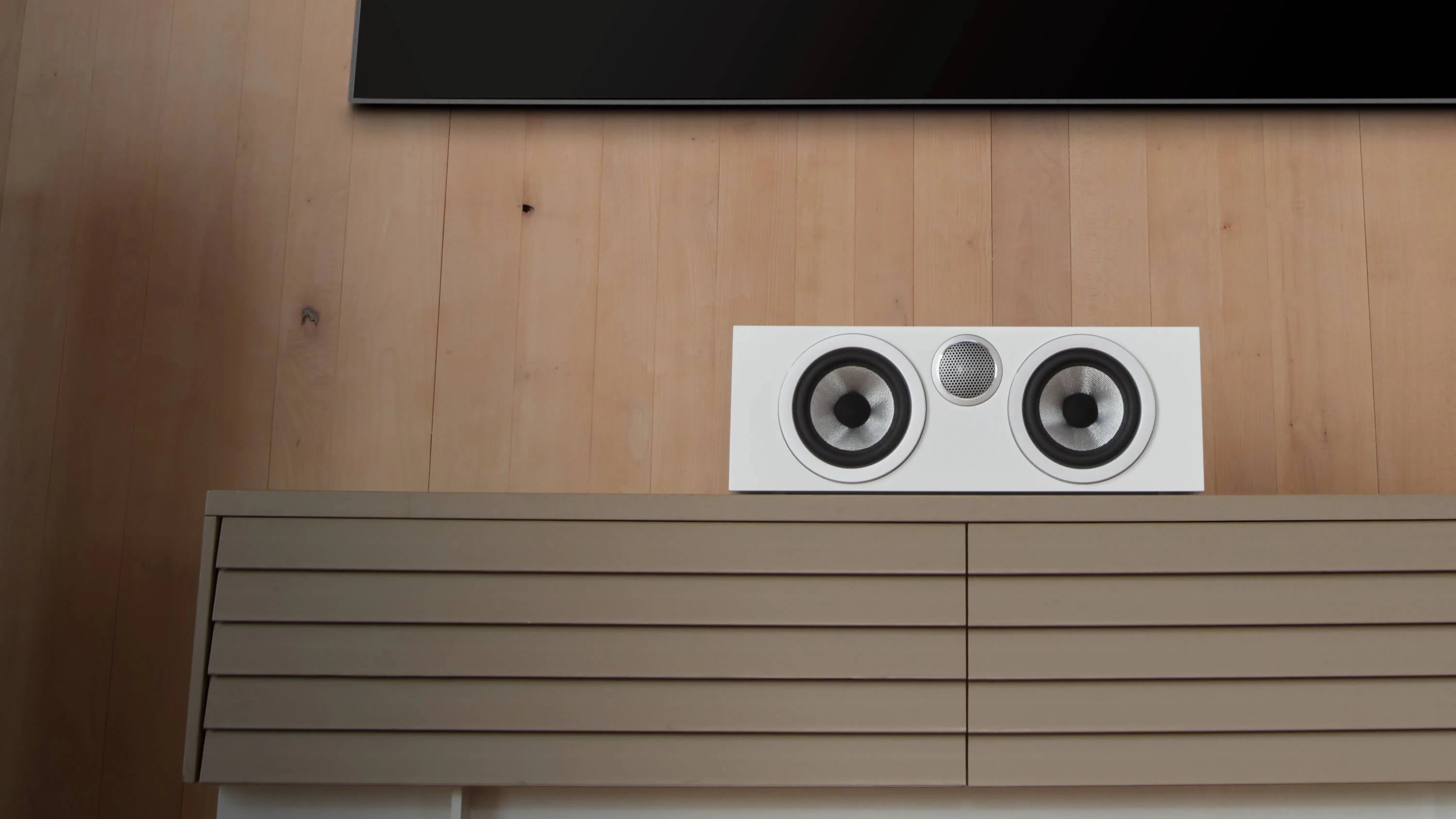 A B&W HTM72 S3 Centre Channel speaker in satin white finish on a TV console in a modern living room.