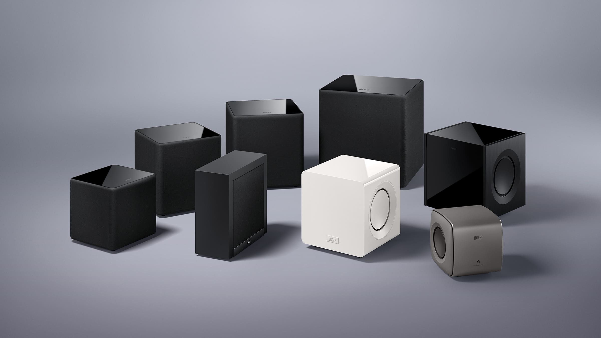 Collection of black and white speakers and KEF KC92 Dual 9” Subwoofer on a gray background