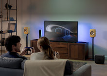 Couple watching TV in a living room with KEF speakers on KEF S1 Floor Stands for LSX II and a cabinet.