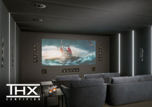 Home theater setup with a large screen displaying a ship scene, surrounded by gray seats and installed KEF Ci3160REFM-THX Reference In-Wall speakers.